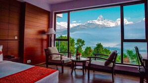 A hotel room with a large window offering a mountain view, a bed, a desk, and two chairs. - Himalayan Front Hotel by KGH Group (Pokhara)