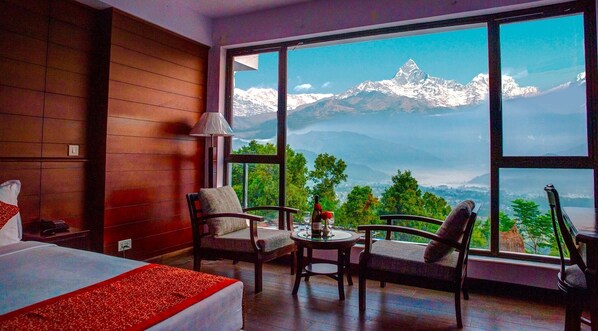A hotel room with a large window offering a mountain view, a bed, a desk, and two chairs. - Himalayan Front Hotel by KGH Group (Pokhara)