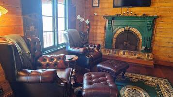 A cozy room with a fireplace, leather armchairs, a television, and a patterned rug.