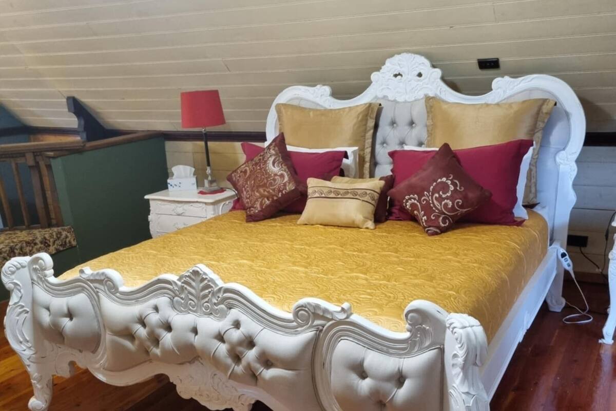 A bedroom with a white ornate bed, a wooden floor, and a red and white patterned rug.