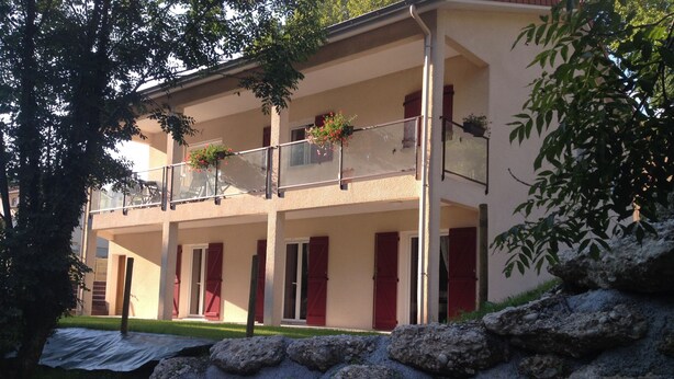 Ein Gebäude mit einer steinernen Fassade, mehreren Balkonen mit roten Fensterläden und einem Garten.