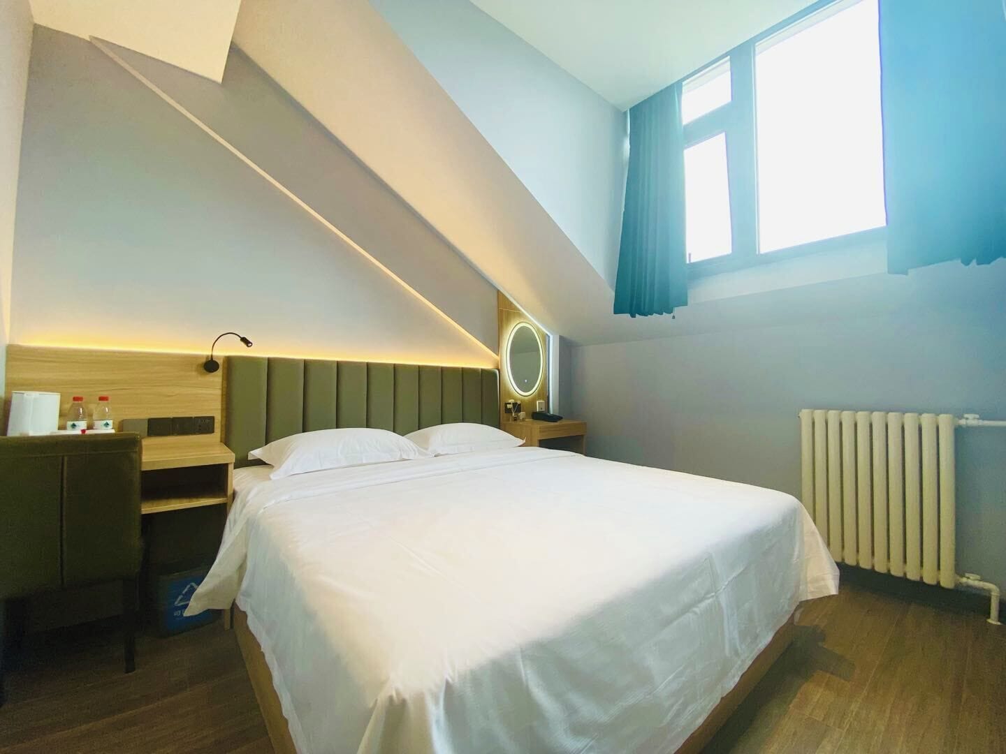 Een hotelkamer met een bed, nachtkastje, lamp en een raam met gordijnen.