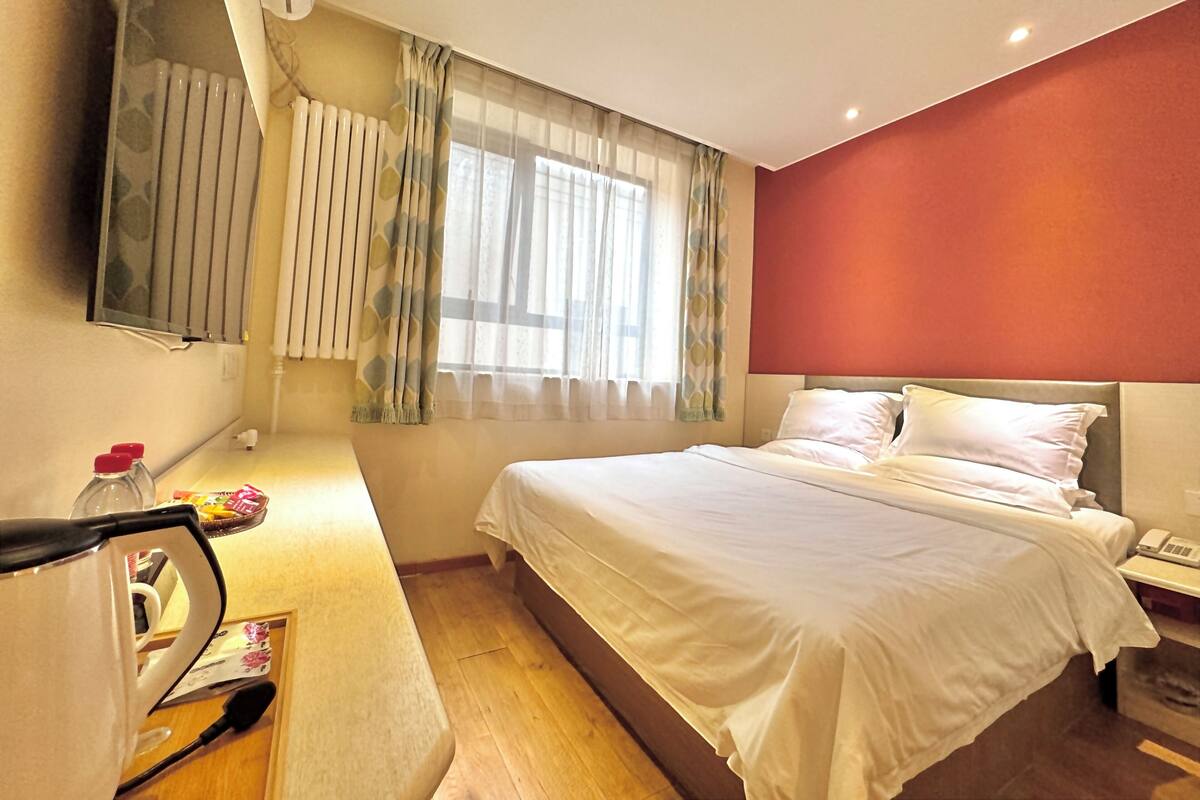 A hotel room with a bed, bedside table, and a mirror.