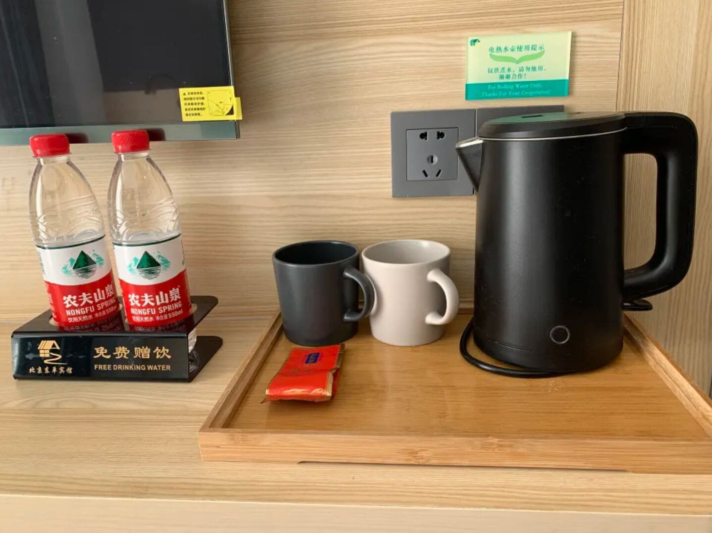 Una bandeja con dos botellas de agua, dos tazas, una tetera y una caja pequeña sobre una superficie de madera.