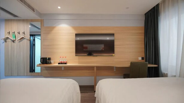 Ein Hotelzimmer mit zwei Betten, einem Holztisch, einem Flachbildfernseher, einer Kaffeemaschine und einer Wasserflasche.