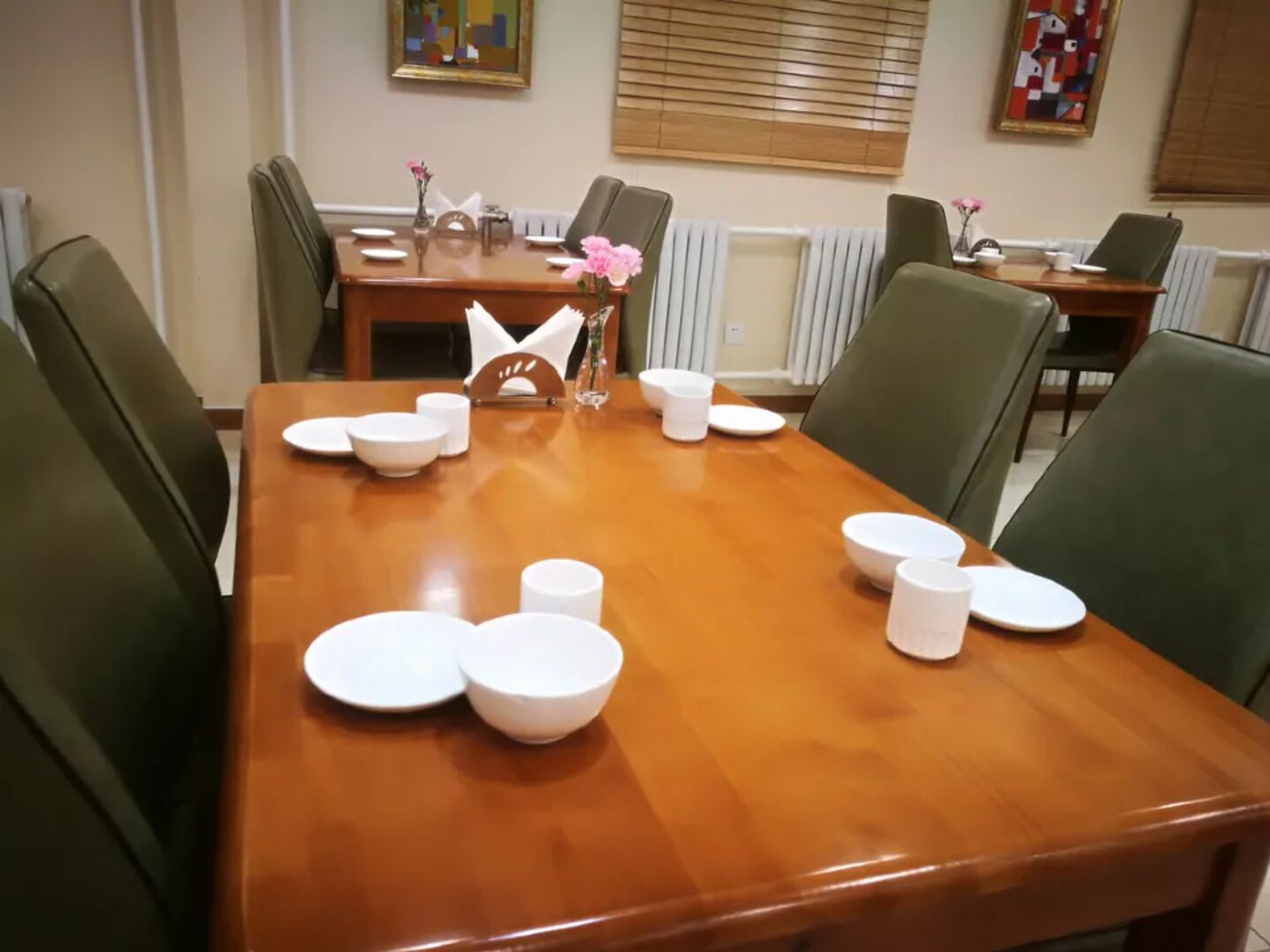 A dining area with a wooden table set for six, surrounded by green chairs.