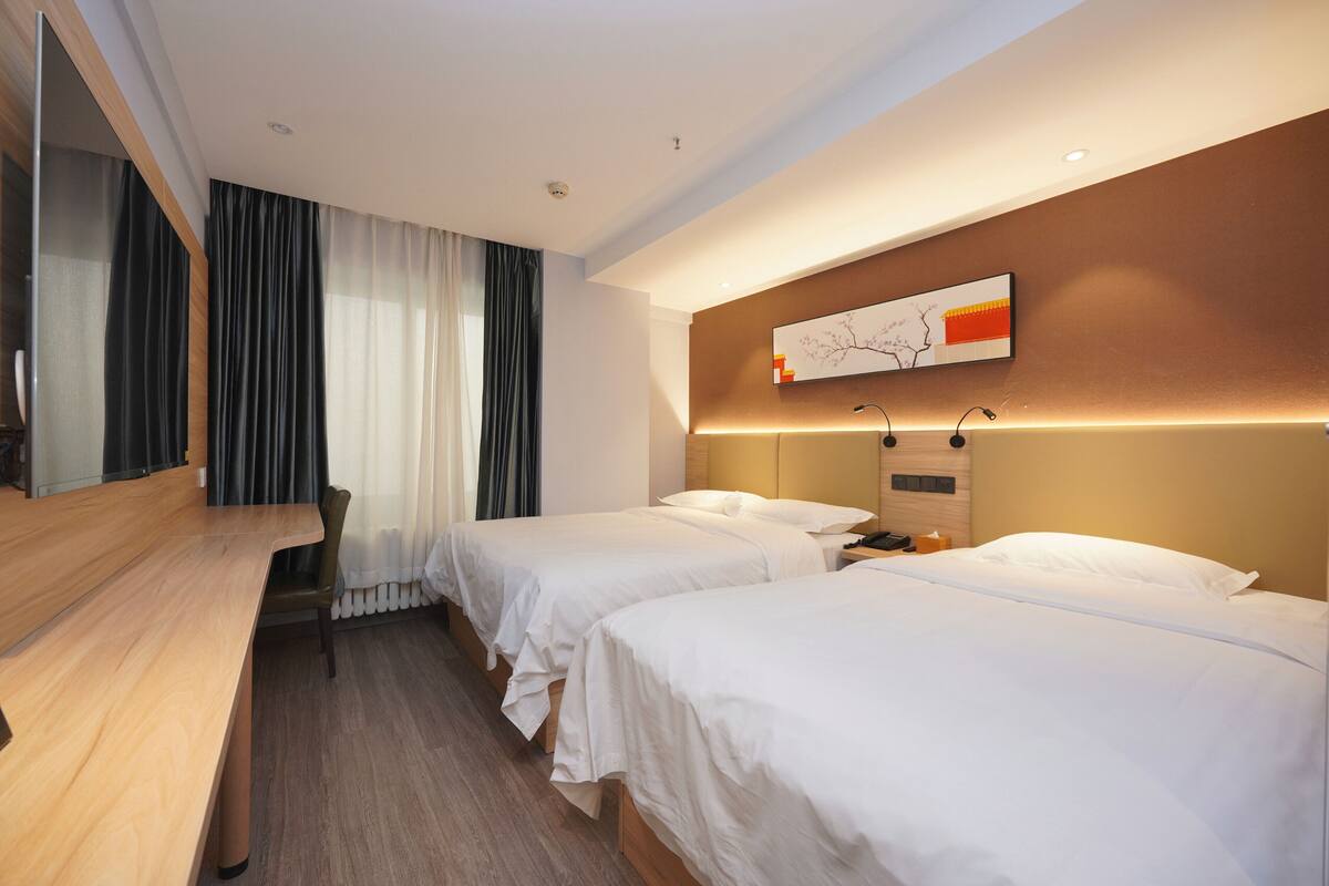 A hotel room with two beds, a desk, and a large window with curtains.