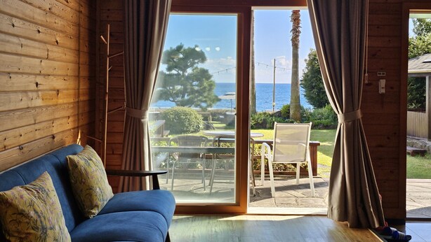 A room with a wooden interior, a blue sofa, and a large window with curtains. - Old Man and Sea Pension (Seogwipo)