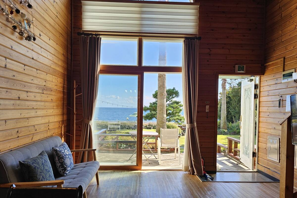 A wooden cabin with a large sliding glass door leading to an outdoor patio with a view of the sea.
