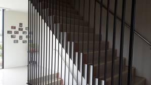 A modern staircase with a metal railing, a wall with framed pictures, and a bright interior. - Apartment Khunpa (Koh Samui)