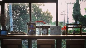 A table with a framed picture, a clock, and a vase with red flowers. - Apartment Khunpa (Koh Samui)