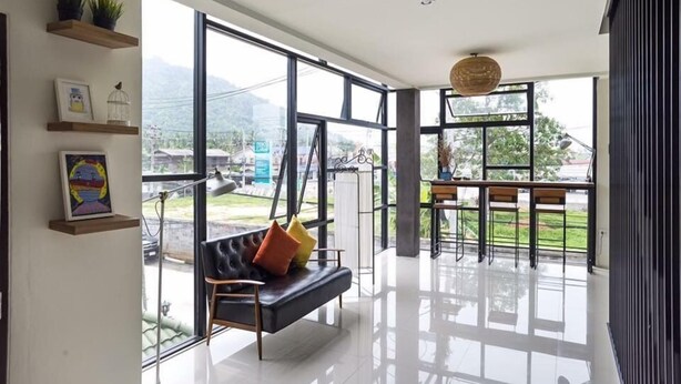 A spacious room with a large window, a black sofa with colorful cushions, and a dining area with a table and chairs. - Apartment Khunpa (Koh Samui)