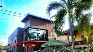 A modern building with a glass facade, a red awning, and a green roof. - Apartment Khunpa (Koh Samui)