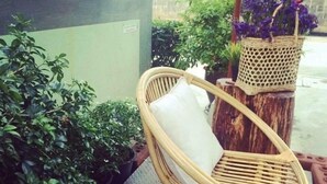A wicker chair with a white cushion in an outdoor area with potted plants and a wicker basket with purple flowers. - Apartment Khunpa (Koh Samui)