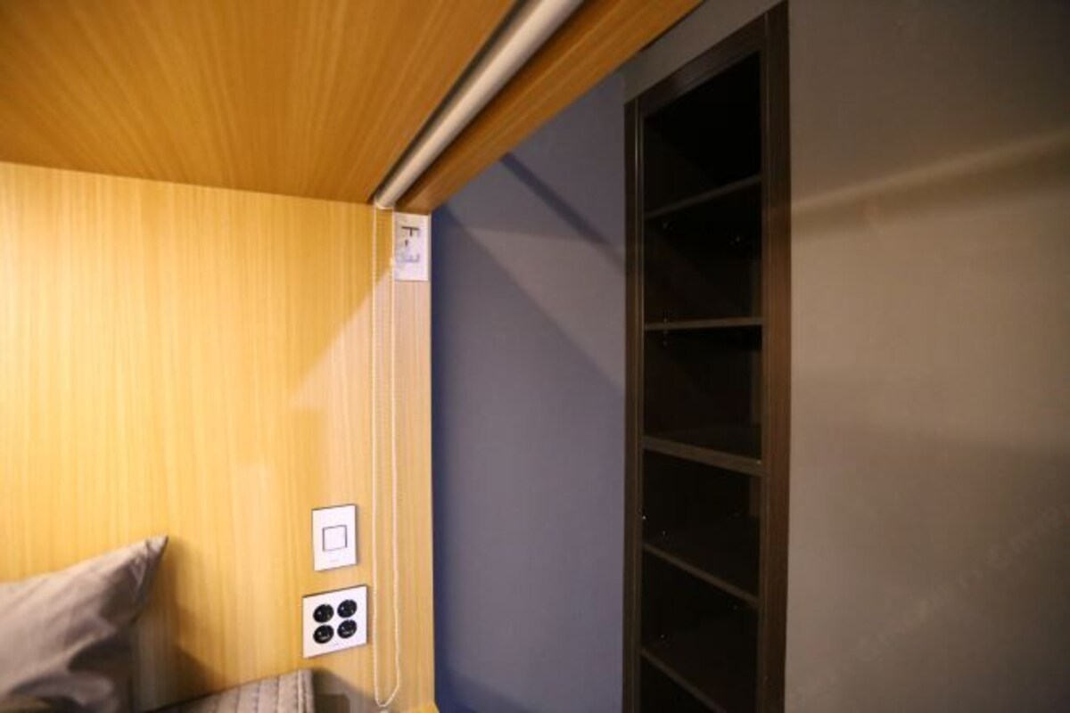 Une pièce avec un plafond en bois, une fenêtre avec des stores, un interrupteur fixé au mur et une prise de courant.