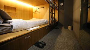 A compact hotel room with a single bed, a small wardrobe, and a shoe rack.