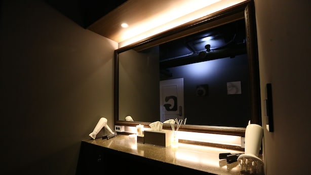 A hotel bathroom with a large mirror, a sink, a telephone, and a tissue box.