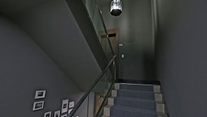 A staircase with a glass railing, a wooden door at the top, and a hanging light fixture.