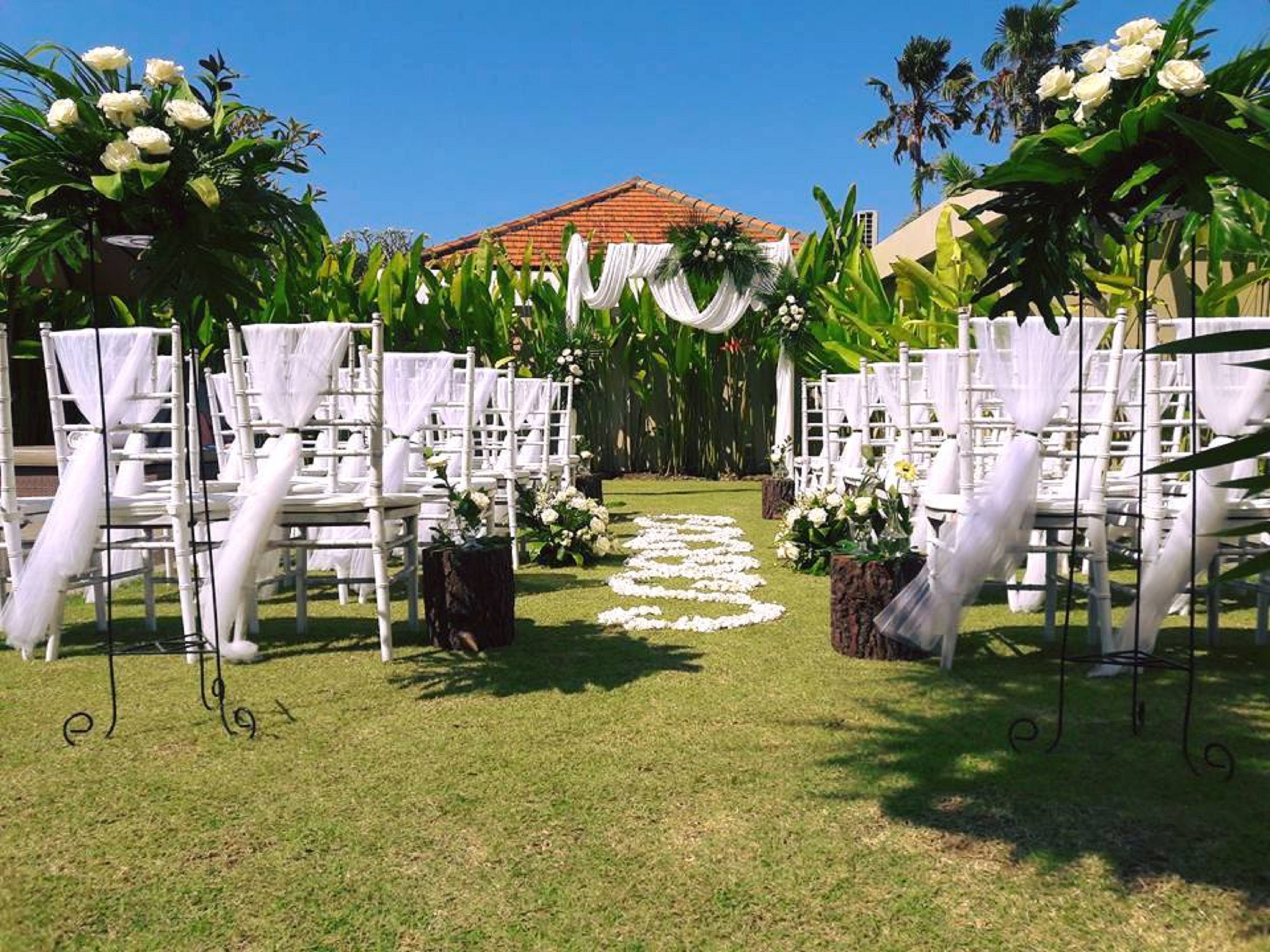 An outdoor wedding venue with white chairs and a grassy aisle.