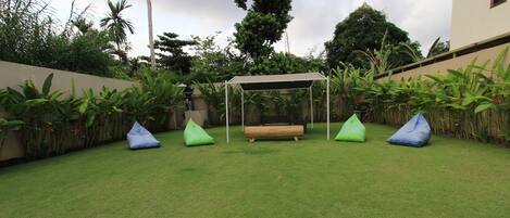 Um quintal bem cuidado com um banco de madeira, área de estar coberta e poltronas de bean bag verdes.