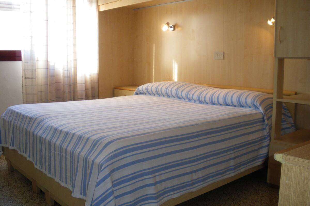 Una cama individual con una colcha a rayas en una habitación con paredes y cabecera de madera.