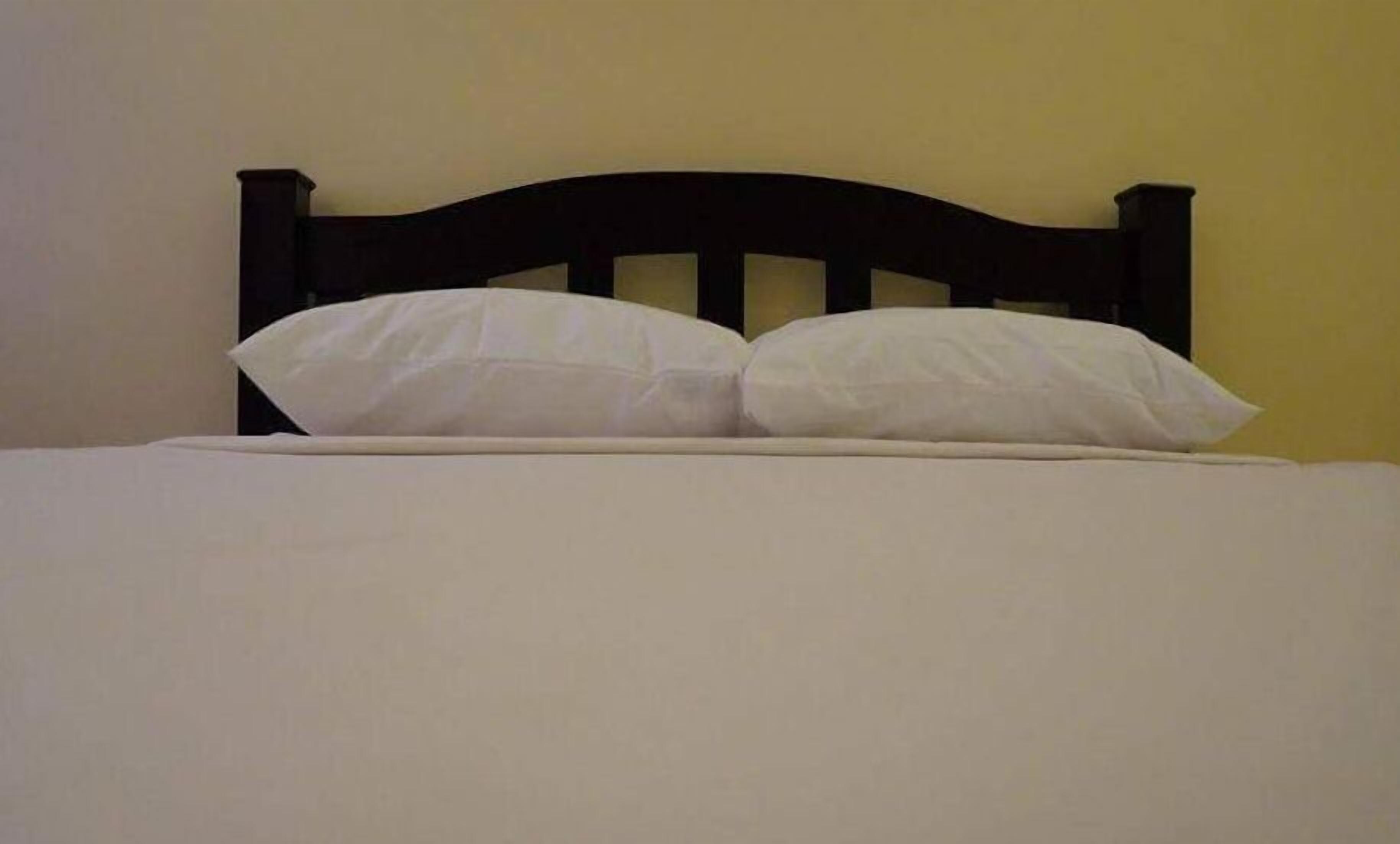 Cama com cabeceira escura e duas almofadas brancas.
