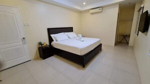 Een slaapkamer met een bed, nachtkastje, deur en een luchtverkoeler aan de muur.