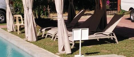 Zona de piscina con sillones de descanso y una zona de estar cubierta.