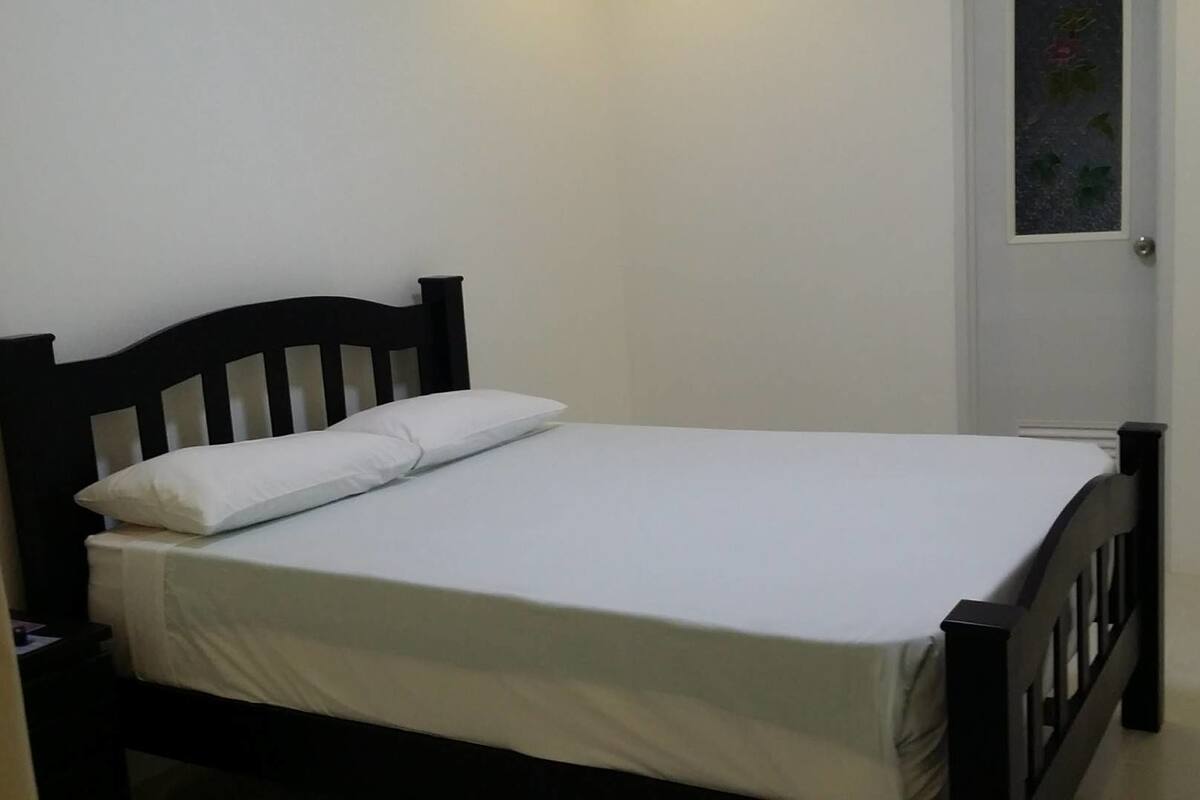 A single bed with a wooden headboard and white bedding in a room with plain walls and a door with a window.