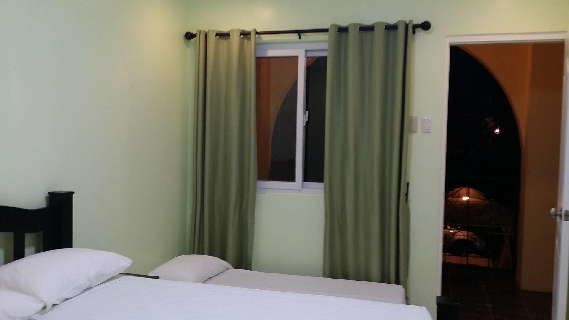 A bedroom with a bed, a window with curtains, and a door leading to a balcony.