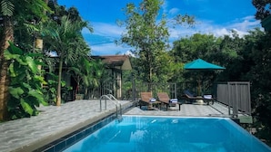 A swimming pool with lounge chairs and a covered area, surrounded by lush greenery and trees. - Hotel Yo (Kandy)