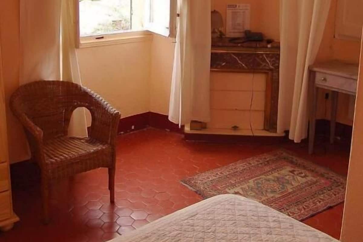A bedroom with a bed, a chair, a desk, and a window with curtains.