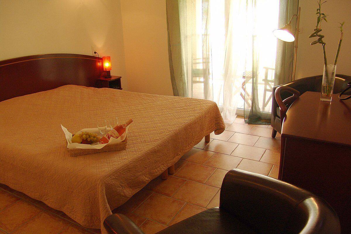 A hotel room with a bed, a bedside table with a lamp, a chair, and a small table with a vase.