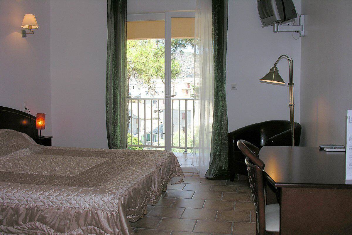 A bedroom with a bed, a desk, a chair, a lamp, and a TV.