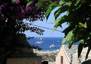 Vista costera con barcos, un muro de piedra y un edificio con techo inclinado.