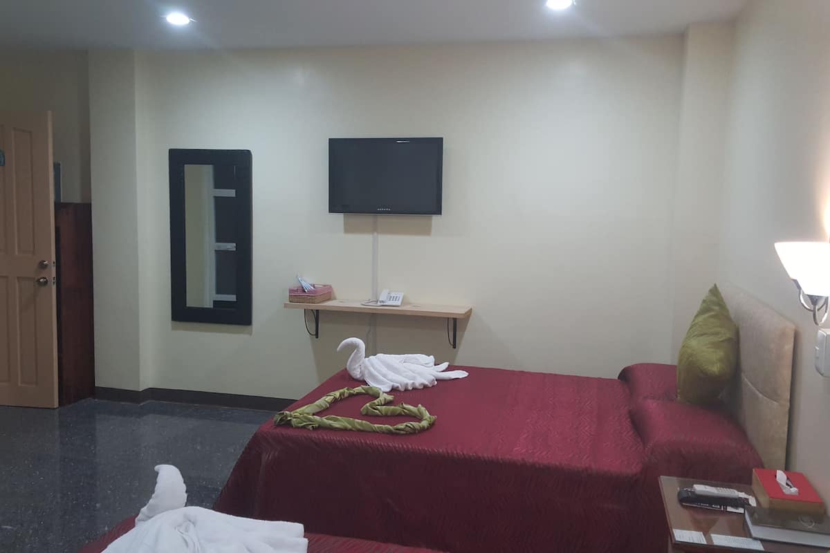 A hotel room with a bed, a desk, a flat-screen TV mounted on the wall, a door, and a mirror.