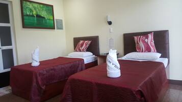 Two single beds with red bedspreads and matching pillows, complemented by a framed landscape painting.