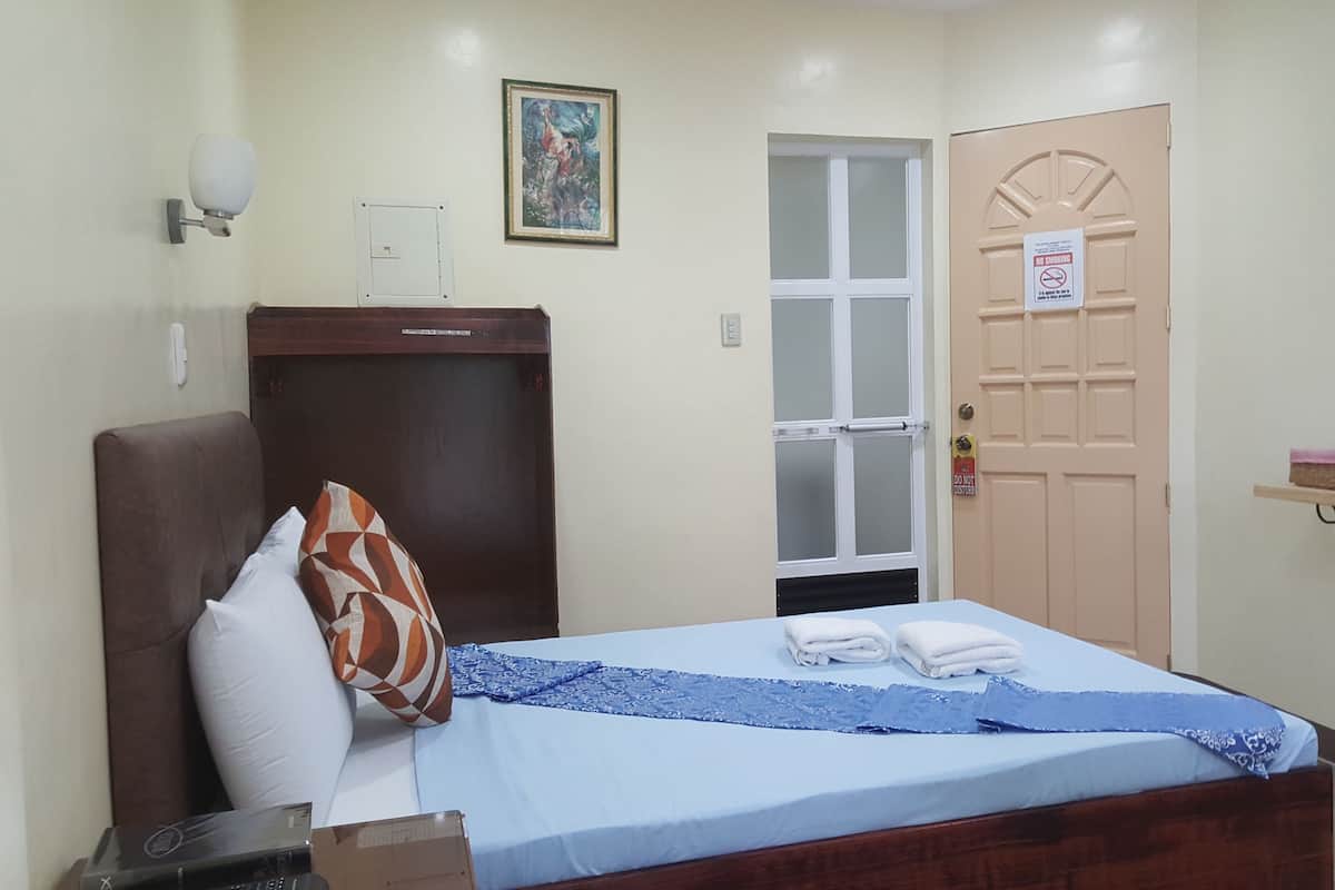 A hotel room with a bed, a wardrobe, a door, and a small shelf with items.