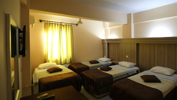 Una habitación de hotel con cuatro camas individuales, una mesita pequeña con un control remoto y una cortina.