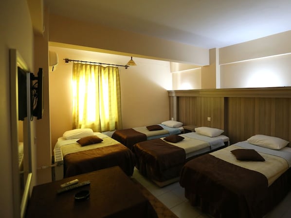 Une chambre d’hôtel avec quatre lits simples, une petite table avec une télécommande et un rideau.