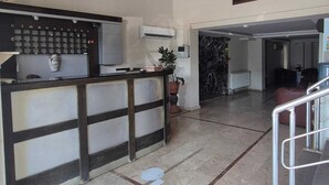 A reception area with a counter, a painting on the wall, and a marble floor. - Cihanay Hotel (Antalya)