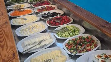 Buffet com diversas opções de comida, incluindo frutas, legumes, queijos e azeitonas.
