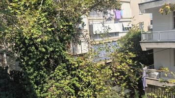 Una zona residencial con edificios de varios pisos, follaje denso y un balcón con barandilla.