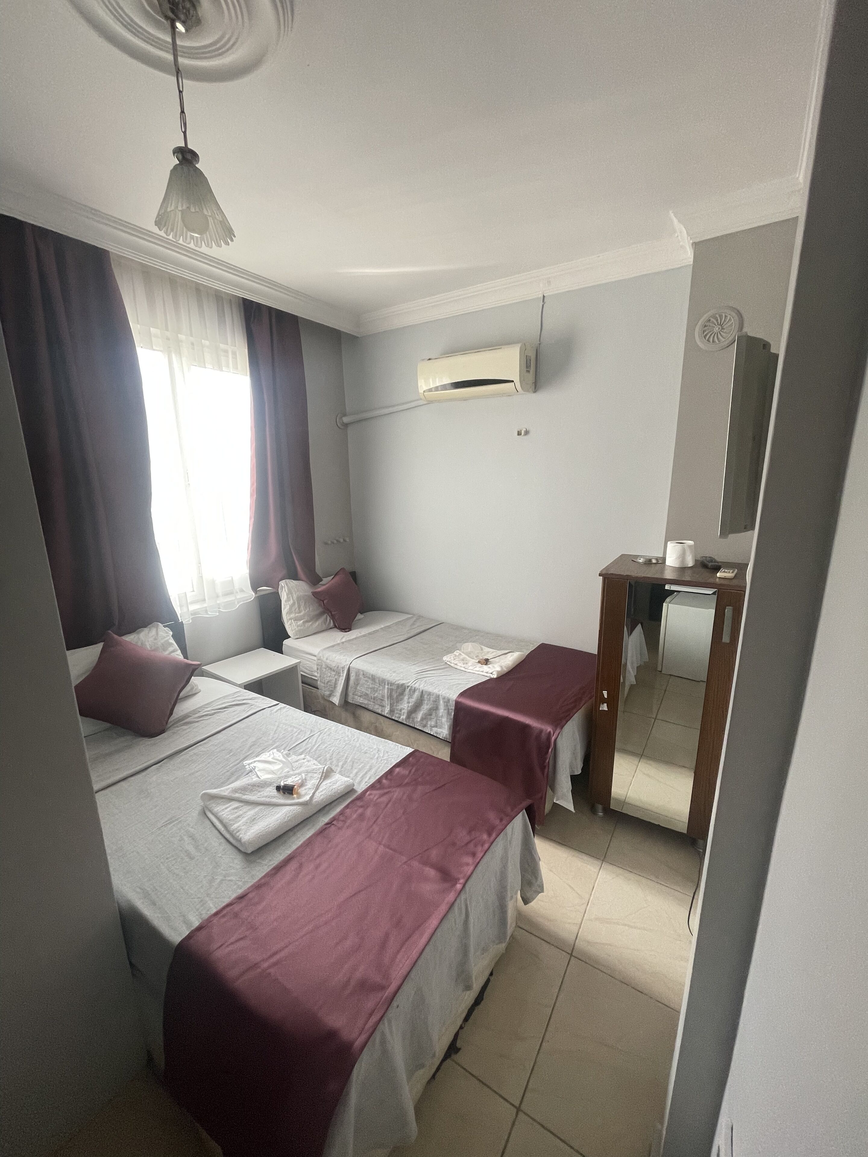 A hotel room with two beds, a desk, a mirror, and an air conditioning unit.