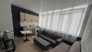 A modern living room with a sofa, a dining table, and a kitchen area with wooden cabinets and a washing machine. - Ersoy Aga Otel (Antalya)