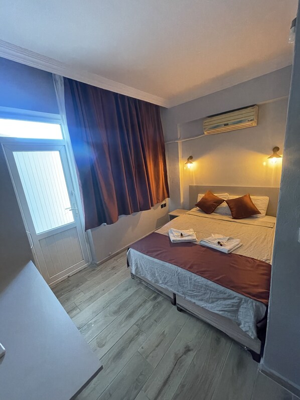 Una camera da letto con un letto, una finestra con tende, un comodino e un condizionatore d'aria a parete.