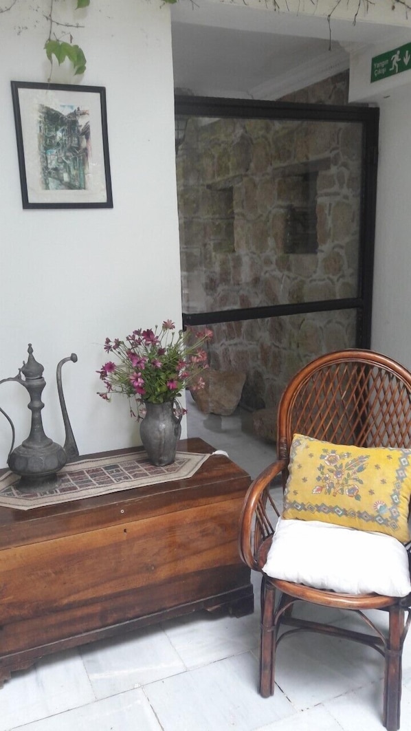 Un coin avec un banc en bois, une chaise avec un coussin jaune, un vase de fleurs, un tableau encadré et un mur en pierre.