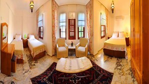 Habitación de hotel con dos camas, un rincón de descanso con sillas, una mesita pequeña y un tapete decorativo.