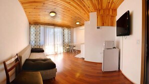 Una habitación acogedora con techo de madera, un sofá, una silla, una mesita y un televisor en la pared.