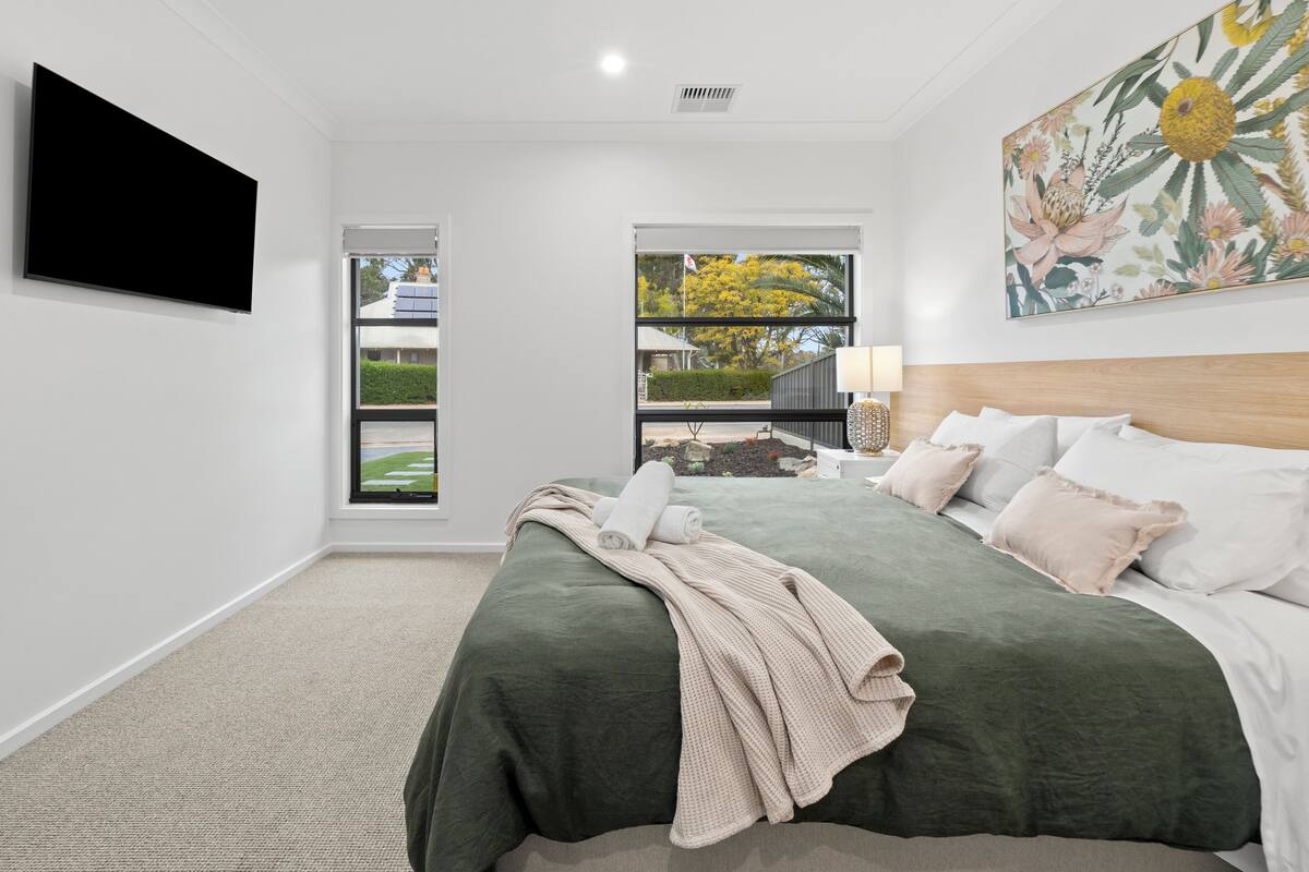 Un dormitorio con una cama grande, un televisor de pantalla plana montado en la pared y una ventana con vistas al exterior.